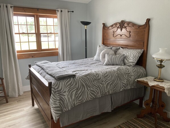 Ein Schlafzimmer mit einem hölzernen Bett, bettenbezügen mit ZEBRA-MUSTER, einer Nachttischlampe und einem Fenster mit Vorhängen.