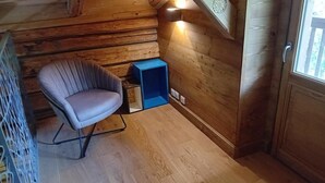 A wooden cabin interior with a cushioned chair, a small blue cabinet, and a wooden door. - LE Chalet Favre - Hauteluce (HAUTELUCE)