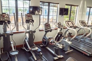 A gym with various exercise machines, large windows, and a television mounted on the wall.