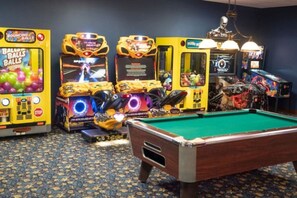 A pool table in a room with arcade games and a patterned carpet.