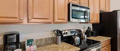 A kitchen with wooden cabinets, a stainless steel microwave, a stove, and a refrigerator.