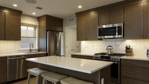 Une cuisine moderne avec des meubles en bois, des appareils électroménagers en acier inoxydable et un îlot central doté de tabourets.
