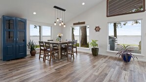 A spacious dining area with a wooden table and chairs, large windows offering a view of the water, and a blue cabinet. - Perfect Lakehouse ~Dock w/ 2 slips ~Kayaks ~Ramp (Pittsburg)