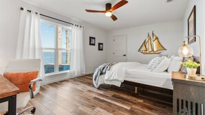A bedroom with a wooden floor, a bed with white bedding, a desk with a chair, a ceiling fan, and a window with curtains. - Perfect Lakehouse ~Dock w/ 2 slips ~Kayaks ~Ramp (Pittsburg)