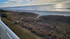 Une vue sur la plage, avec une terrasse en bois et des dunes herbeuses.