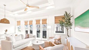 Una sala de estar moderna con un sofá blanco, sillas de madera, una mesa redonda y un ventanal con persianas.