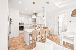 A modern kitchen with white cabinets, a central island with bar stools, and pendant lighting.