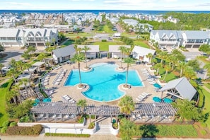 A resort with a central swimming pool, sun loungers, and a view of the ocean.