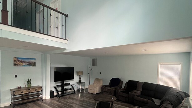 A spacious living room with a high ceiling, a staircase, and a large window.