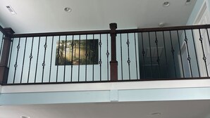 A spacious living area with a dining table, chairs, and a chandelier. There is a staircase with a railing leading to an upper level.