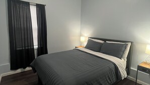 A bedroom with a bed, two bedside tables, a window with curtains, and a ceiling light.