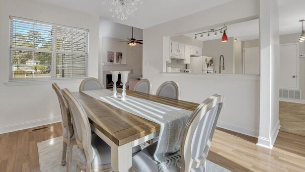Comedor con mesa de madera, sillas blancas, una araña y vista de la cocina a través de un arco.