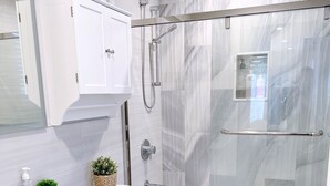 Un baño moderno con ducha envuelta en vidrio, inodoro blanco y tocador con lavabo y almacenamiento.