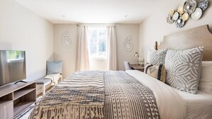 Un dormitorio con cama, televisión, escritorio y ventana con cortinas.