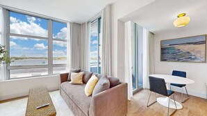 Ett modernt vardagsrum med ett stort fönster, en soffa, ett matbord och en tavla på väggen.