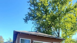 Una cabaña de madera con un amplio ventanal corredera, un porche pequeño y un césped bien cuidado.