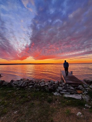 A person walking on a wooden pier extending into a body of water during sunset.