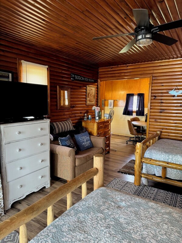 Interior acogedor de una cabaña con techo de madera, televisor, sofá con cojines, escritorio y cama.