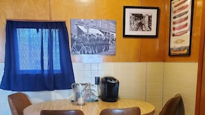 Un pequeño comedor con una mesa redonda y cuatro sillas, una máquina de café y una fotografía enmarcada en la pared.