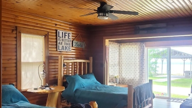 Una cabaña con dos camas de madera, un ventilador de techo y un letrero que dice 'La vida es mejor en el lago'.