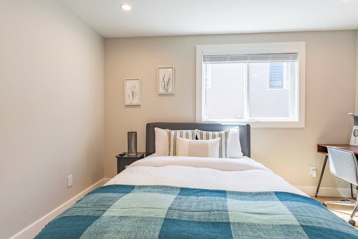 Un dormitorio con cama, mesita de noche, escritorio y ventana.