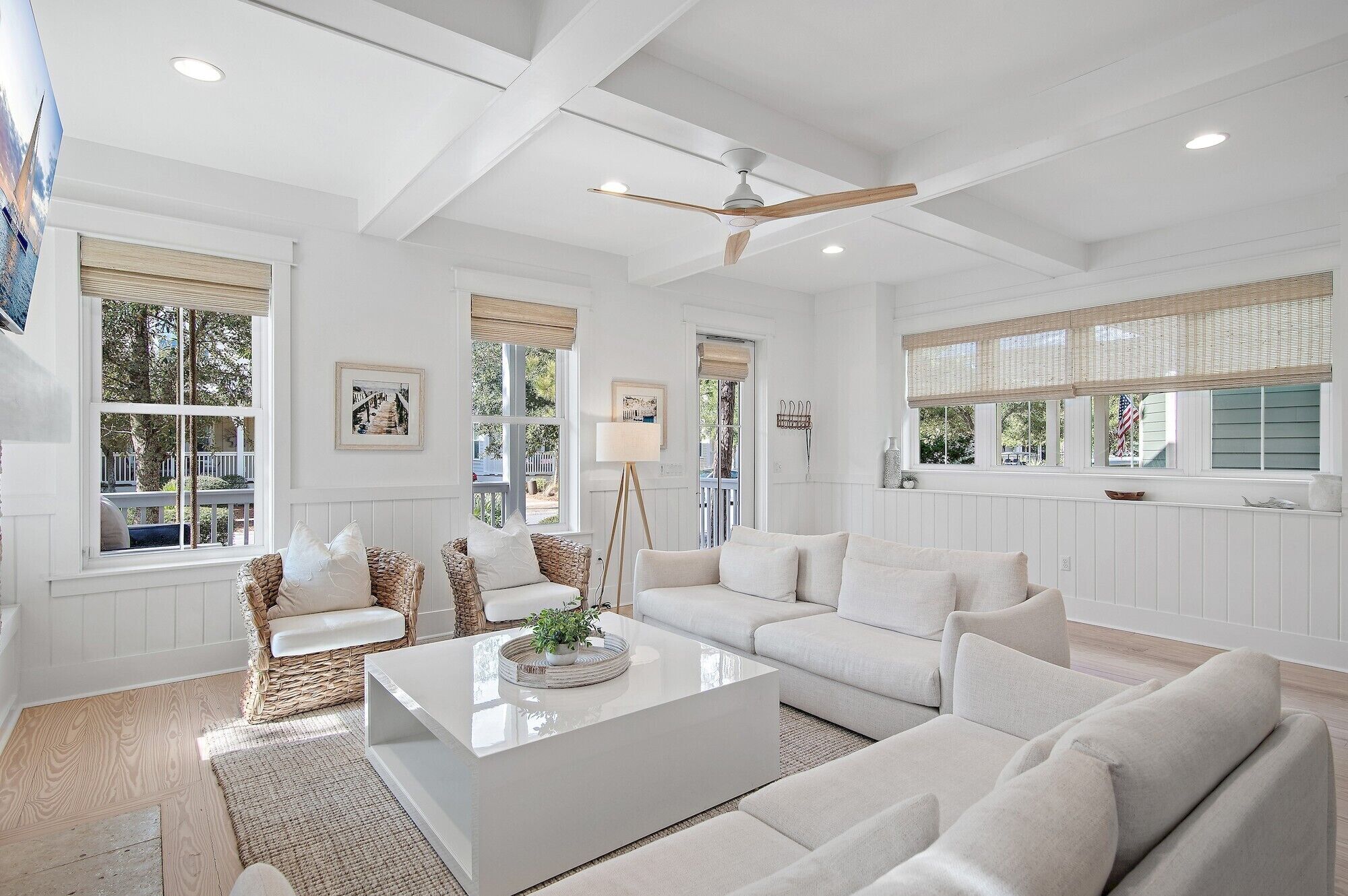 A spacious living room with white furniture, large windows, and a ceiling fan.