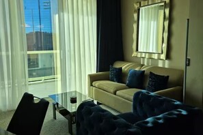 A modern living room with a sofa, a glass coffee table, and a view of the city through large windows.