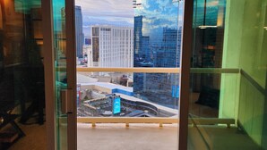 Uitzicht vanuit een hotelkamer met een glazen deur naar een balkon. Het balkon biedt zicht op een stadsbeeld met hoogbouw en een heldere lucht.
