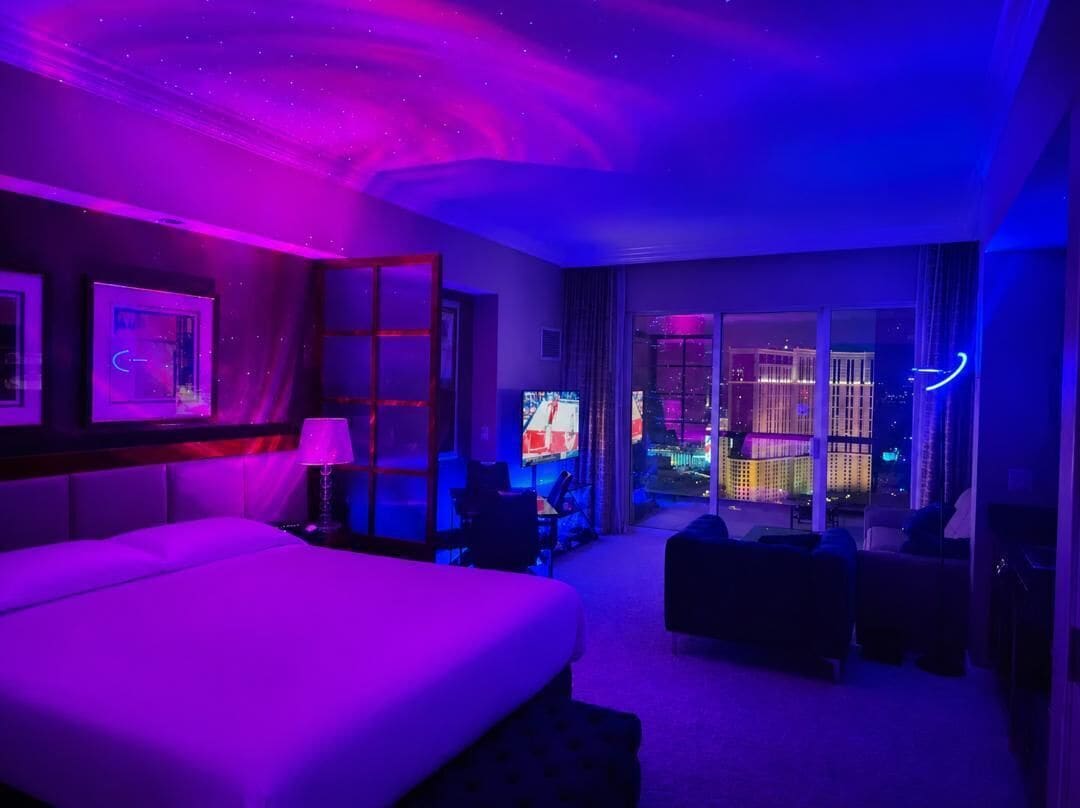 Een hotelkamer met een bed, een bureau, een stoel en uitzicht op de stad.