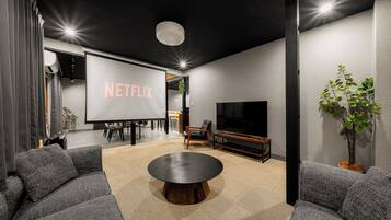 A modern living room with a large flat-screen TV, a Netflix sign, comfortable seating, and a coffee table.
