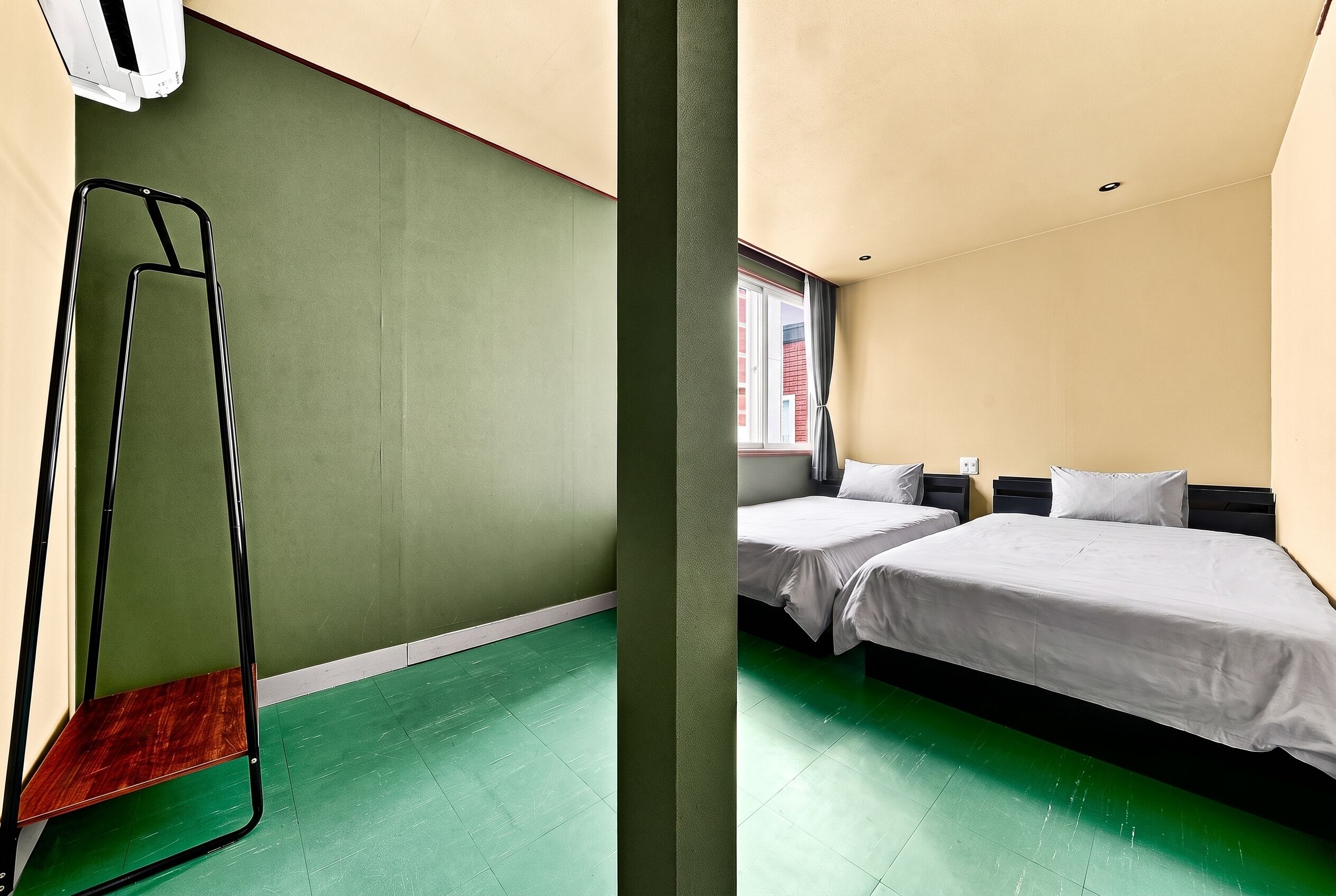 A hotel room with two beds, a green floor, and a window with a view.