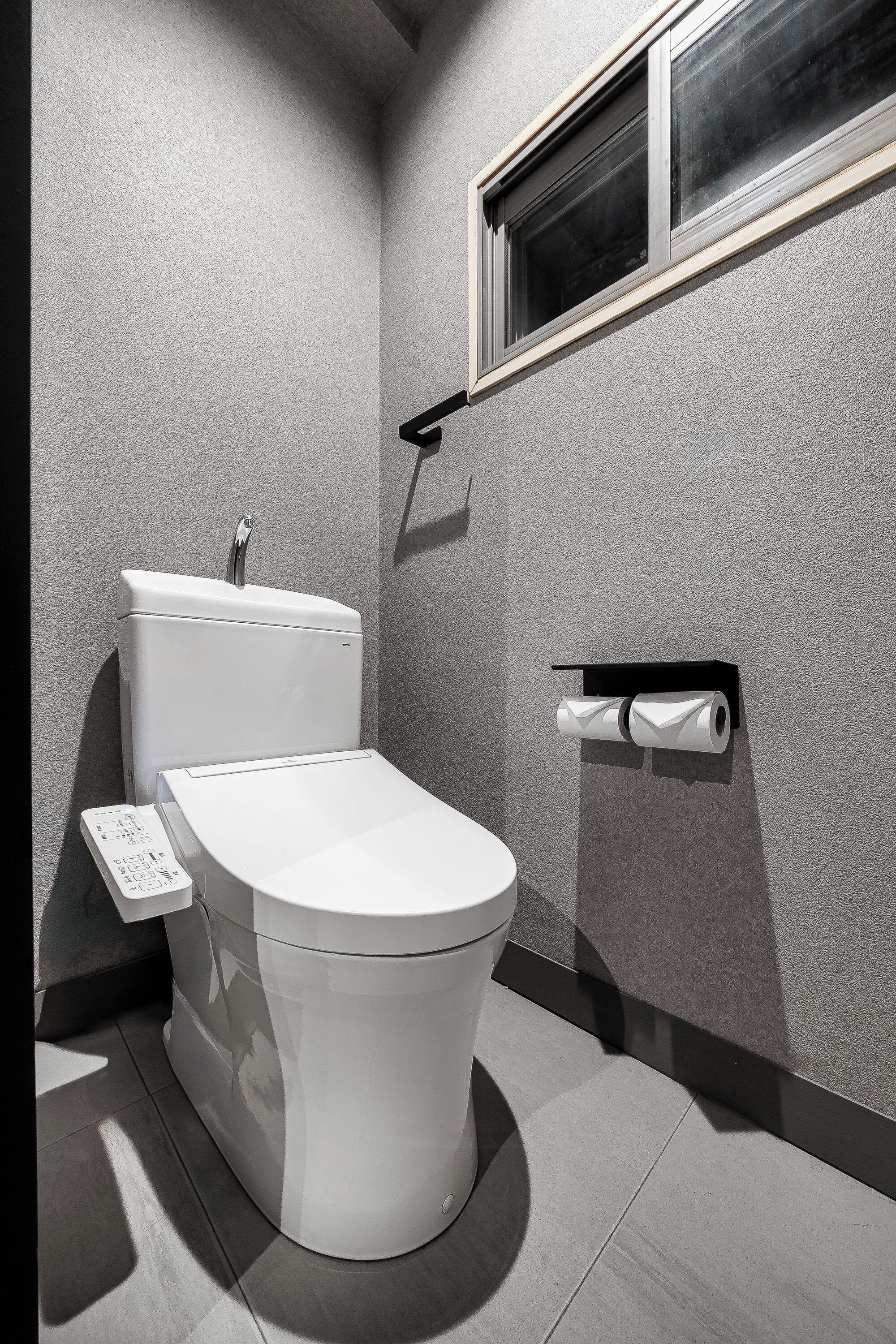 A modern bathroom with a toilet, a hand dryer, and a toilet paper holder.