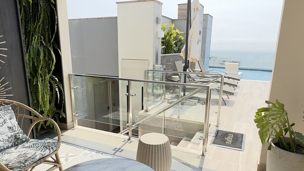 A balcony with a glass railing, a round table, and two wicker chairs. - Peru & Barranco, Food and History (Barranco)