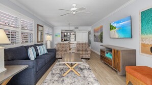 Un salon moderne avec un canapé bleu foncé, des fauteuils à motifs, une table basse en bois et un ventilateur de plafond.