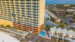 A high-rise hotel with multiple floors, a swimming pool, and a beach view.