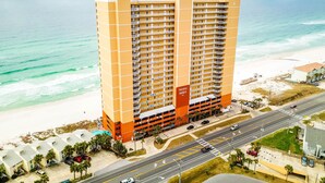 A high-rise hotel with multiple balconies, a parking garage, and a beach view.