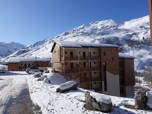 Ein mehrstöckiges Gebäude mit verschneitem Dach, eingebettet in eine Berglandschaft mit schneebedecktem Boden und Felsen.
