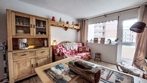 Una habitación acogedora con un armario de madera, un sofá con una manta roja y blanca, una cafetera y una ventana con vistas a edificios.