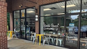 Fachada de tienda con letrero de cafetería infantil, mesas al aire libre y diseño de ladrillo.