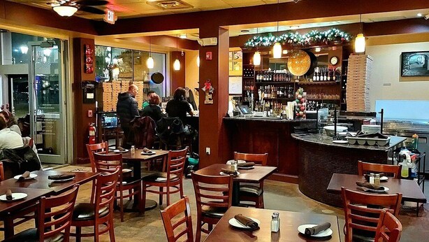 Un restaurante con mesas y sillas de madera, una zona de bar y vistas al océano.