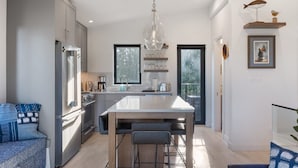 A modern kitchen with a central island, stainless steel appliances, and a hanging light fixture. - Saratoga Sands at THE BEACH HOUSE (Campbell River)
