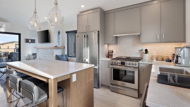 A modern kitchen with stainless steel appliances, a central island with bar stools, and pendant lighting. - Saratoga Sands at THE BEACH HOUSE (Campbell River)