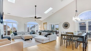 Ein großzügiges Wohnzimmer mit einer breiten Couch, einem Esstisch für sechs Personen und einem durch einen offenen Durchgang einsehbarer Küchenbereich.