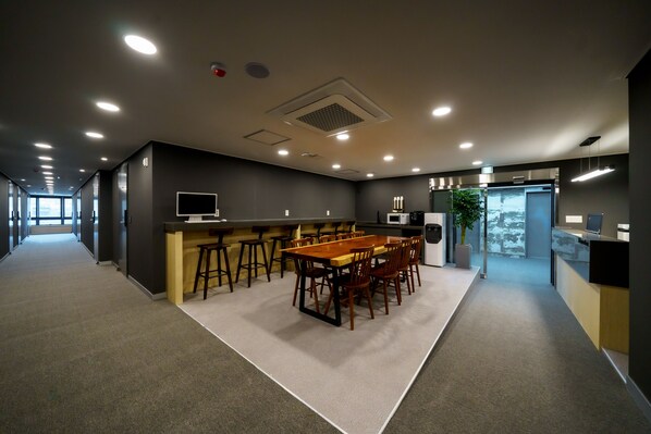 A modern conference room with a long table and chairs, a bar area, and a kitchenette.