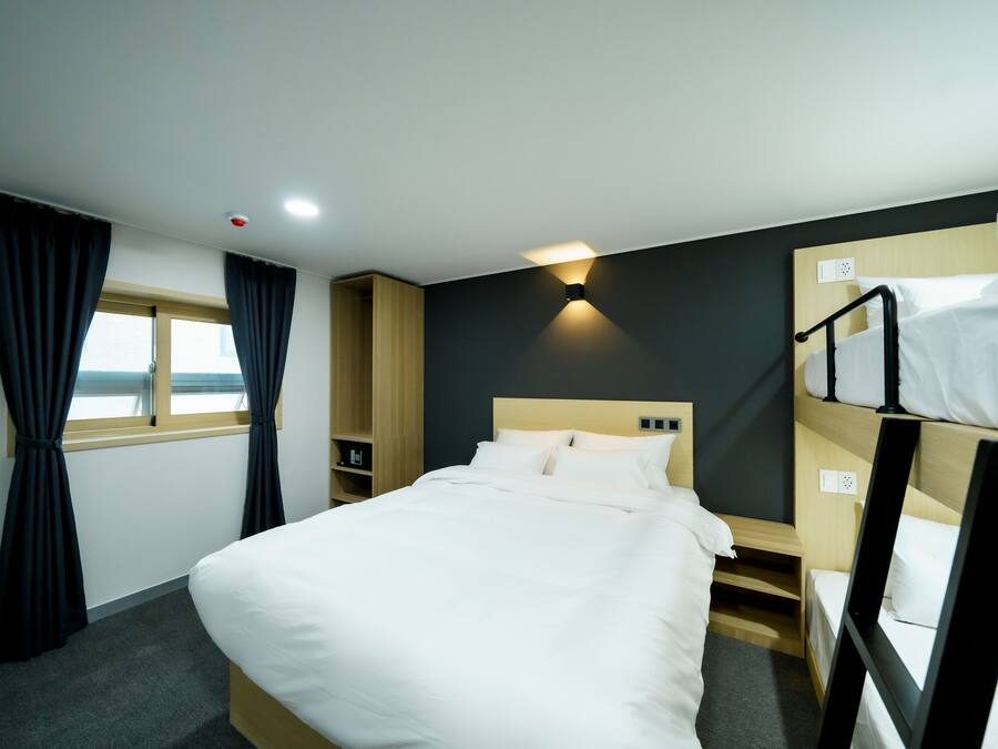A hotel room with a single bed, a wooden nightstand, a small shelf, and a window with curtains.