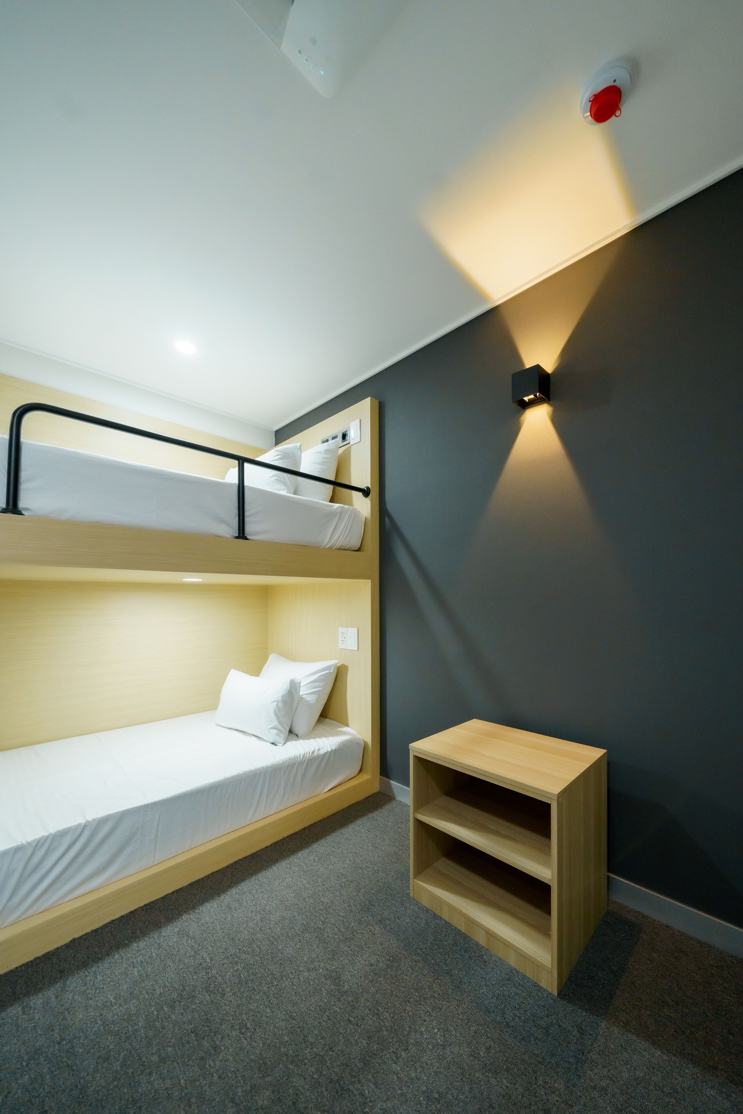 Habitación con literas, un pequeño estante de madera y una lámpara fijada a la pared.