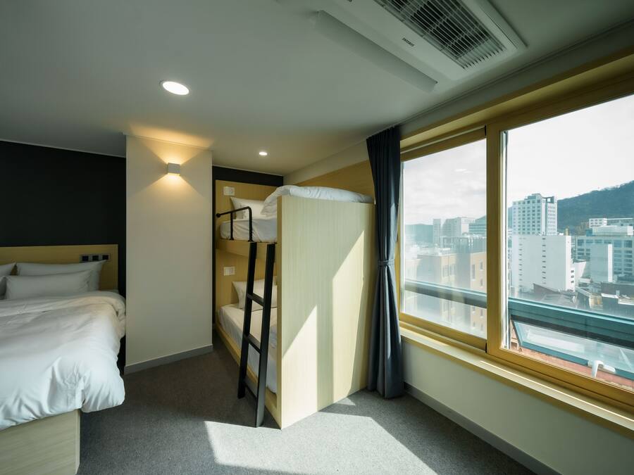 Habitación de hotel con literas, una cama individual, ventana con vista a la ciudad y un respiradero en el techo.