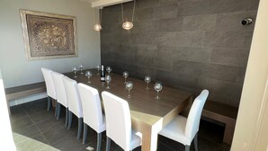 Een eetgedeelte met een lange tafel, witte stoelen en verschillende wijnglazen.