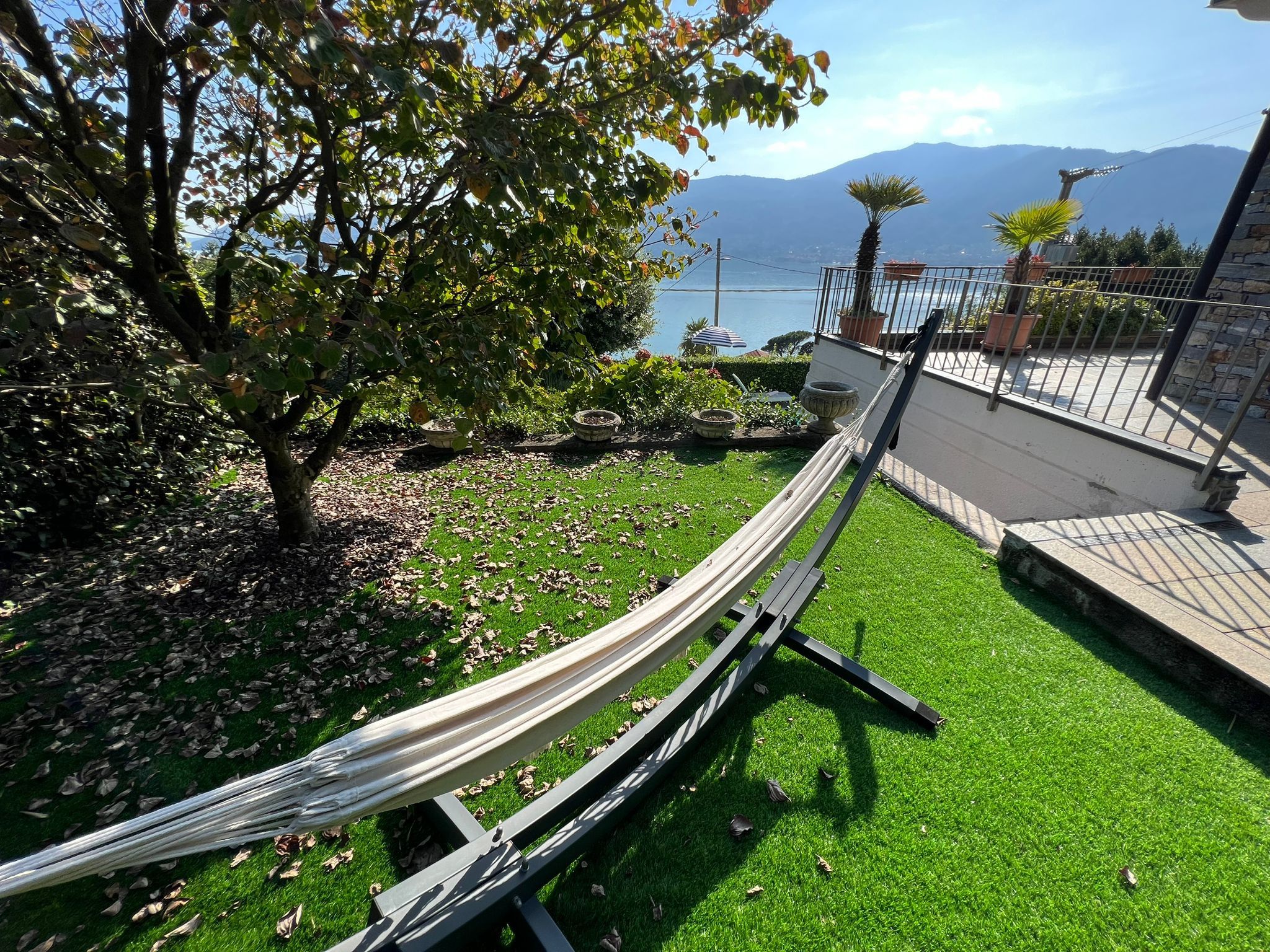 A hammock on a green lawn with a view of a lake and mountains.