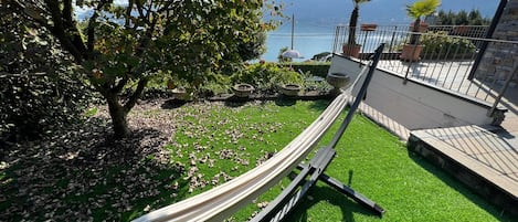 A hammock on a green lawn with a view of a lake and mountains.
